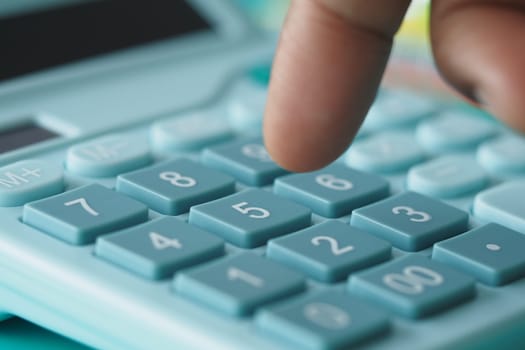 A finger is pressing the number 5 button on a light blue calculator with various functions