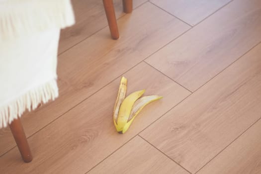 A wilting banana rests despondently on a light wooden floor adjacent to white fabric