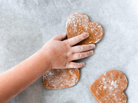Childs hand decorating heart shaped cookies on baking sheet.