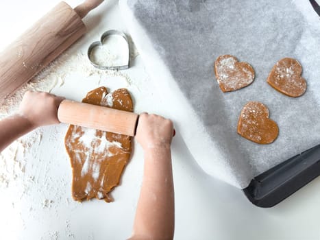 Child rolling dough for heart shaped cookies on baking tray.