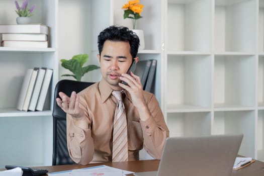 Confident businessman engaged in a phone negotiation, showcasing strong communication while seated at a modern desk with financial documents and a laptop.