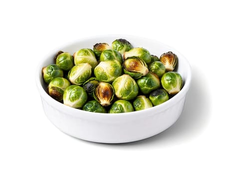 Roasted Brussels sprouts, individual green sprouts browned on edges, glistening with oil, piled in white dish, isolated.