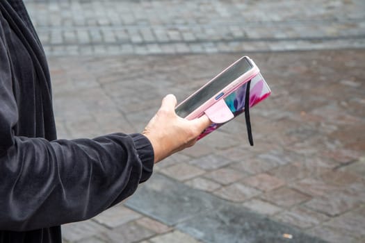 unrecognizable woman in black blouse uses smartphone in pink case on the street in the city, unlimited internet access,