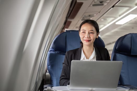 Businesswoman using a laptop on a plane, combining work and travel seamlessly.