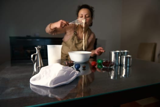 Woman in an apron mixing a bowl of batter on a table filled with ingredients. Fresh produce and tools for cooking are displayed beside her, symbolizing holiday traditions and cheerful preparations.