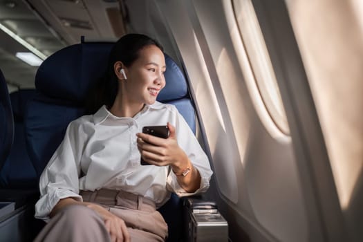 Businesswoman on a plane, using a smartphone, enjoying a comfortable flight. Perfect for travel and business themes.