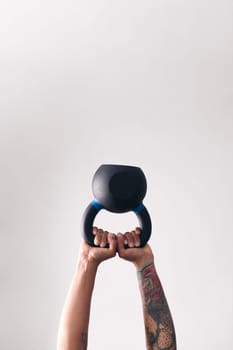 hands of strong woman with tattoos lifting heavy kettlebell white training in gym against white wall, , concept of fitness and active lifestyle, copyspace for text