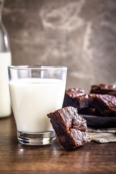 Homemade chocolate brownies and glass of milk on a wooden table.