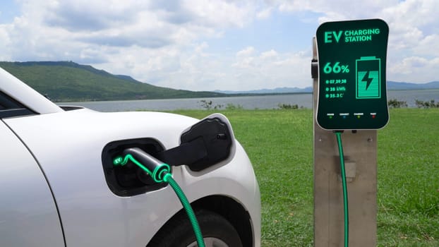 Electric car plugged in with charging station to recharge battery by EV charger cable with nature and lake background. Future innovative ev car and energy sustainability. Peruse