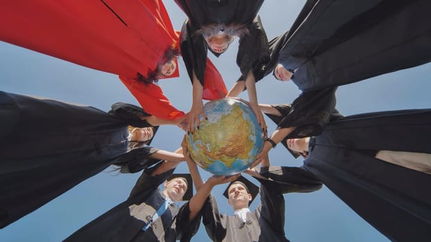 College graduates join hands over a globe of the world overlooking Africa. The concept of world peace