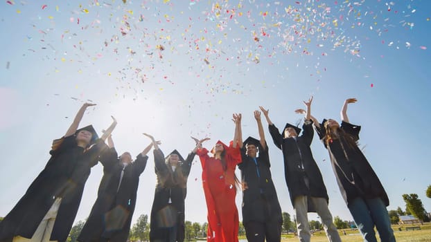 Happy college graduates throw colorful confetti against the rays of sunshine