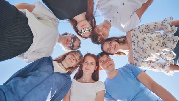 Seven young high school students amicably put their heads together and look down waving their arms