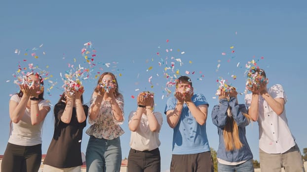 Friends blow colorful paper confetti on a sunny day