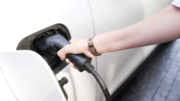 Progressive businesswoman install charger plug from charging station to his electric car before driving around city center. Eco friendly rechargeable car powered by sustainable and clean energy.