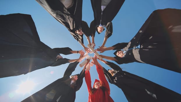 College graduates join hands with diplomas standing in a circle