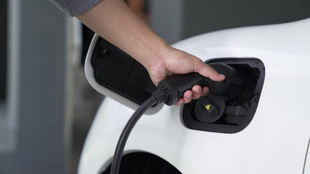 Progressive man attaches an emission-free power connector to the battery of electric vehicle at his home. Electric vehicle charging via cable from charging station to EV car battery