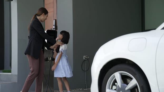 Progressive lifestyle of mother and daughter who have just returned from school in an electric vehicle that is being charged at home. Electric vehicle powered by sustainable clean energy.