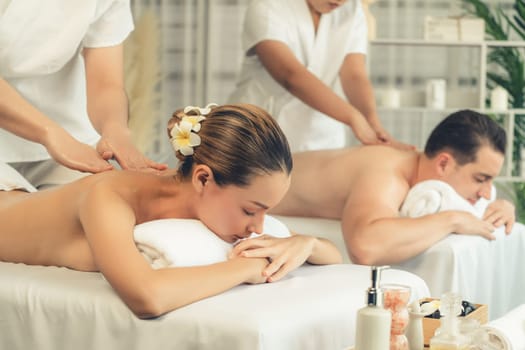 Caucasian couple customer enjoying relaxing anti-stress spa massage and pampering with beauty skin recreation leisure in day light ambient salon spa at luxury resort or hotel. Quiescent