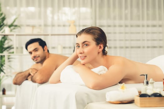 Blissful couple customer having exfoliation treatment in luxury spa salon with warmth candle light ambient. Salt scrub beauty treatment in health spa body scrub. Quiescent