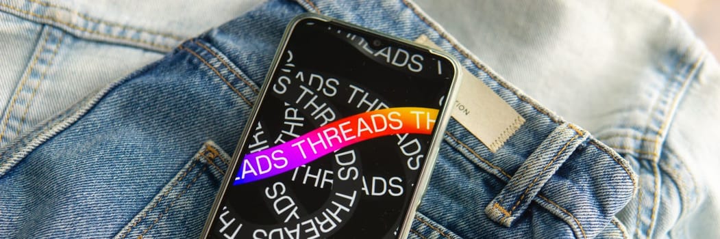 Tver, Russia - July 15, 2023, the threads logo on the smartphone screen lying on the jeans. The threads icon. The logo of the current application. Threads social network