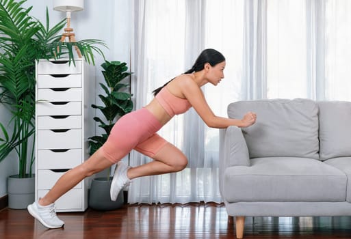 Fit young asian woman stretching her leg her body using sofa in living room. Healthy lifestyle workout training routine at home. Balance and flexibility exercise concept. Vigorous