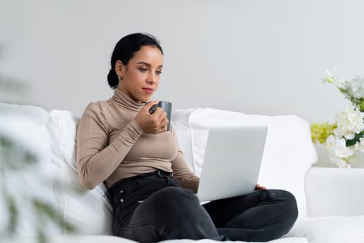 Happy woman drinking coffee on a sofa at home for crucial rest and relaxation. Portrait of young African American woman holding a cup.