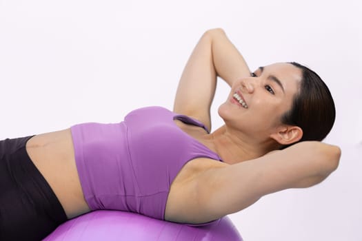 Young attractive asian woman portrait in sportswear with fit ball targeting on abs muscle for effective energetic daily workout routine. Studio shot and isolated background. Vigorous