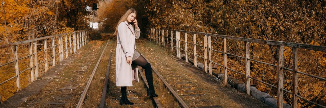 A beautiful long-haired woman walks through the autumn streets. Railway, autumn leaves, a woman in a light coat.