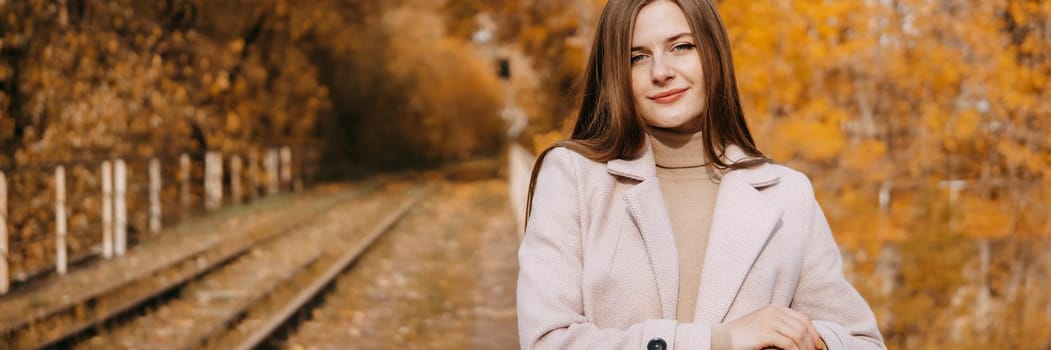 A beautiful long-haired woman walks through the autumn streets. Railway, autumn leaves, a woman in a light coat.