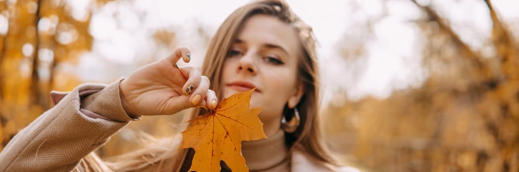 Portrait of a woman with an autumn maple leaf. Railway, autumn leaves, a young long-haired woman in a light coat coat, close-up.