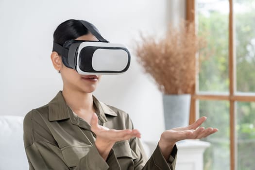 Young woman using virtual reality VR goggle at home for uttermost online shopping experience. The virtual reality VR innovation optimized for digital entertainment lifestyle.