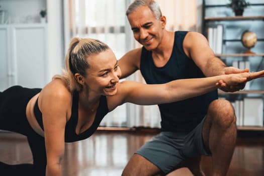 Happy active senior couple in sportswear being supportive and assist on yoga posture together at home. Healthy senior man and woman lifestyle with yoga exercise. Clout