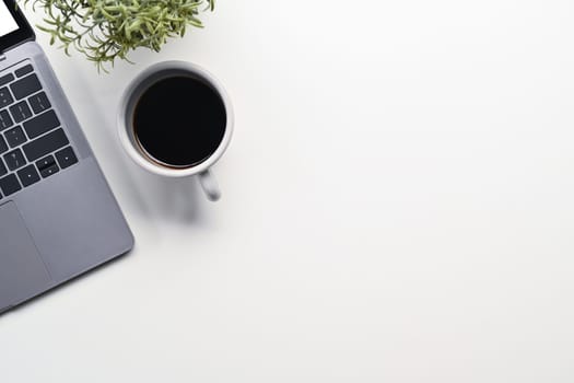 A cup of coffee, laptop and potted plant on white background. Top view with copy space.