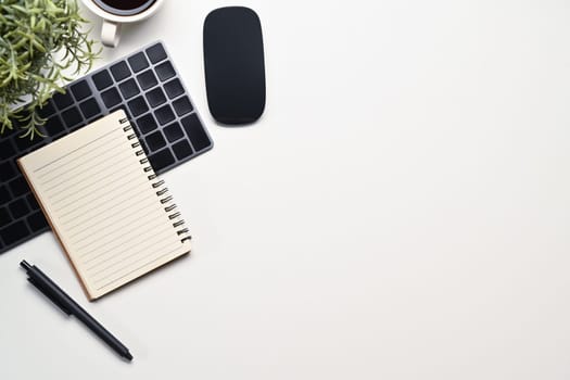 White office desk with wireless keyboard, mouse, notepad and coffee cup. Top view with copy space for text.