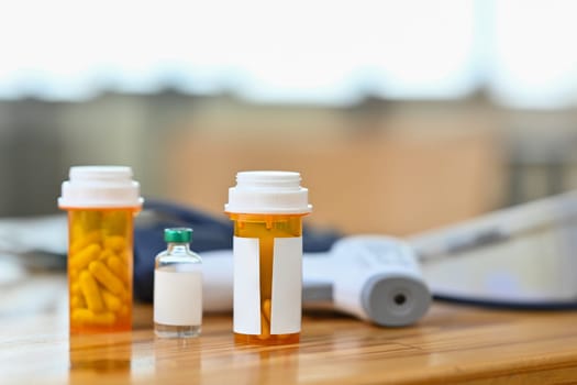 Pills bottles, blood pressure monitor and infrared thermometer on wooden table. Medicine and healthcare concept.