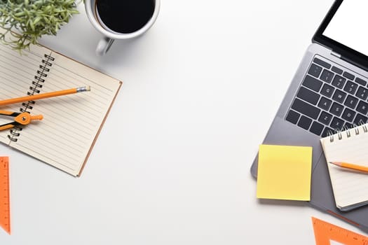 Top view of white office desk with laptop computer, coffee cup and stationery.