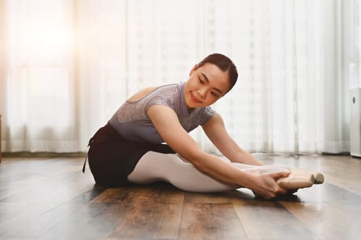 Beautiful young ballerina in pointe shoes doing stretching exercise on the floor. Dance art, education and flexibility concept.