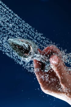 Woman washing silver anal plug under shower on blue background