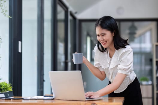 Excited woman holding coffee mug checking work on laptop Feeling cheerful, celebrating success Young woman happy with good email news Inspired by great deals.