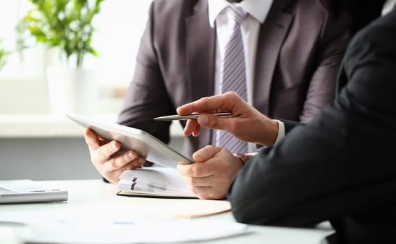 Two businessman are looking and studying statistics on tablet display closeup. Male hand opponent holds pen and points out problem collaboration business coach cooperation partnership palm concept