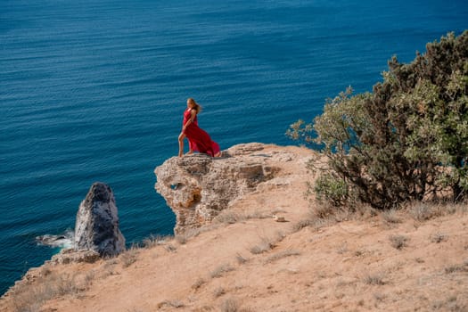 A woman in a red flying dress fluttering in the wind, against the backdrop of the sea