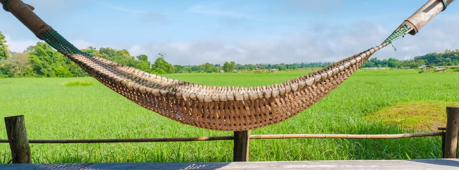 small homestay at the farm with a green rice paddy field in Central Thailand. hammock in front of a wooden bamboo hut looking out over a green rice paddy field in Thailand