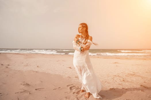 woman sea white dress. Model in boho style in a white long dress and silver jewelry on the beach. Her hair is braided, and there are many bracelets on her arms