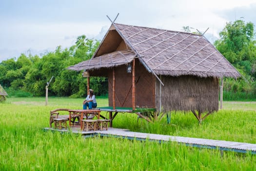 Asian woman on vacation at a small homestay at the farm with a green rice paddy field in Central Thailand