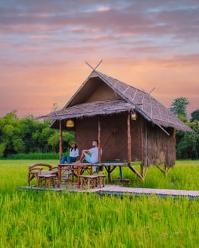 a couple of men and woman at a small homestay on the farm with a green rice paddy field in Central Thailand, young couple on vacation at the Thai countryside