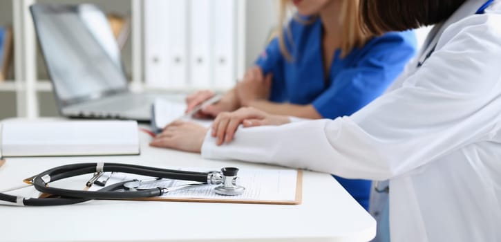 Stethoscope head lying on medical forms closeup while medicine doctor working in background. Patient history list visit check 911 medical calculation and statistics healthy lifestyle concept