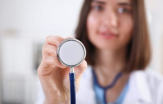 Female medicine doctor hand holding stethoscope head closeup in front of her chest. Medic shop or store physical and disease prevention er consultant 911 pulse measure healthy lifestyle concept