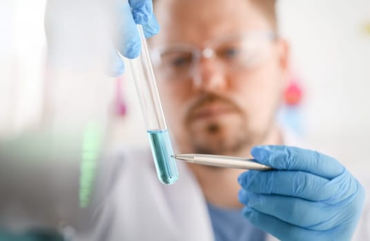 A male chemist holds test tube of glass in his hand overflows a liquid solution of potassium permanganate conducts. Analysis reaction takes various versions of reagents using chemical manufacturing.