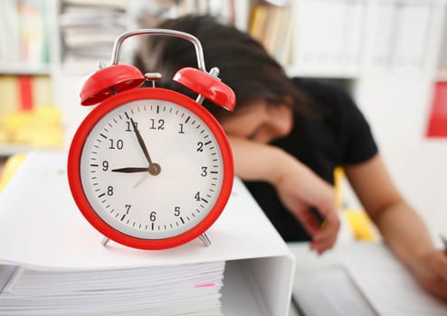 Businesswoman fell asleep in the office connection with processing fatigue. The red alarm clock shows five minutes to nine o'clock morning or evening after the party no strength wake up work normally