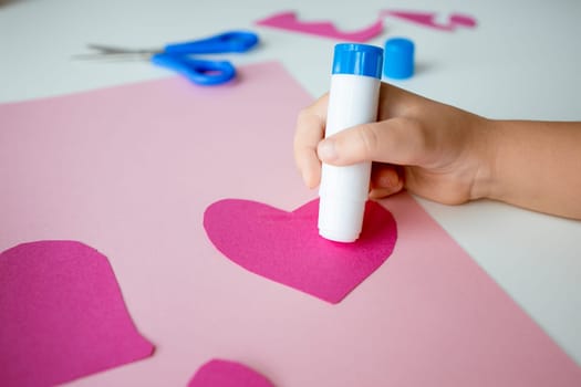 Child crafting heart shapes with pink paper and glue stick.